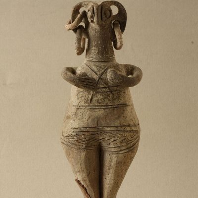 Clay female figurine with a bird-shaped face and disproportionately large ears, from which hang two rows of hoop earrings (22654)